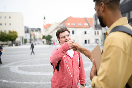 A young man with Down syndrome meeting his mentoring friend in city, fist bumping.の写真素材