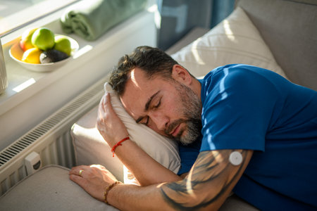 Diabetic man with CGM sensor on arm sleeping on sofa.の写真素材
