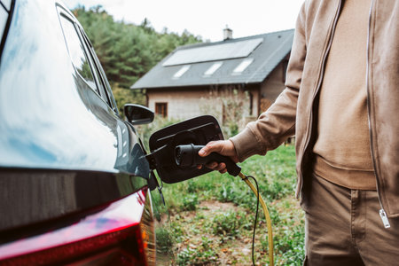 Man charging electric car, plugging charger in charging port.
