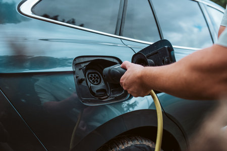 Man charging electric car, plugging charger in charging port.