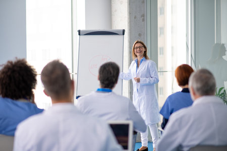 Female doctor as speaker at conference for healtcare workers, medical team sitting and listening presenter. Medical experts attending an education event, seminar in board room.の写真素材