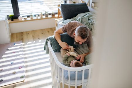 Father putting the baby to sleep, lying next to him in the crib.の写真素材