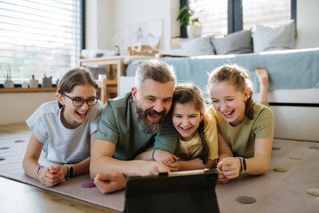 Portrait of father with three daughters watching tv show on tablet.