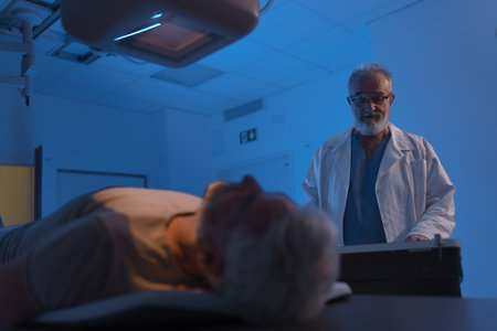 Radiologist performing X-ray examination on male patient using tilting radiographic wall stand.