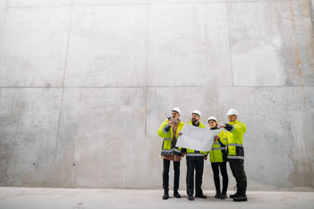 Team of engineers and construction workers reviewing blueprints, building site.の写真素材