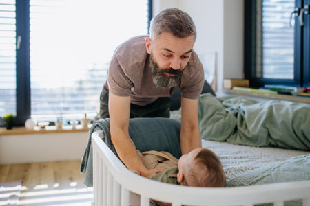 Father putting the baby to sleep, lying him down in crib.の写真素材