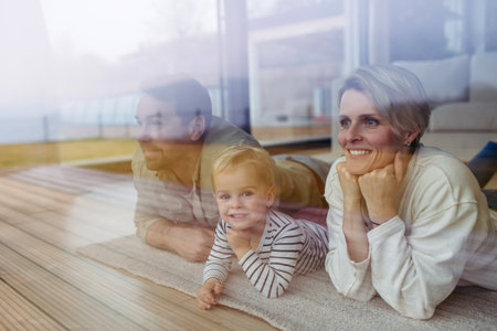 Parents looking out of window with little son, lying on floor.