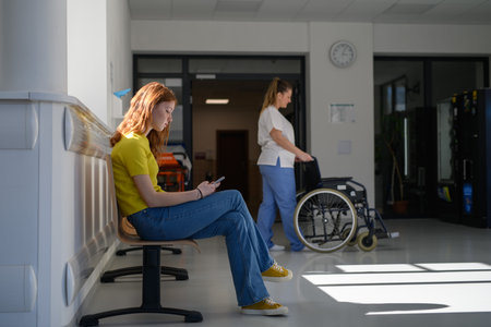 Teenage girl waiting alone in hospital waiting area, scrolling on phone.の写真素材