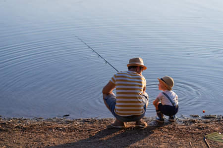 Dad teaching his little boy how to fish by the lakeの写真素材