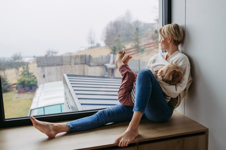 Mother breastfeeding her toddler son by the windowの写真素材