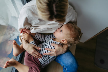Mother breastfeeding her toddler son by the windowの写真素材