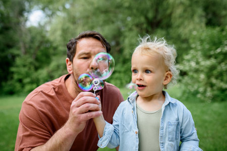 Father and son blowing soap bubbles in park.の写真素材