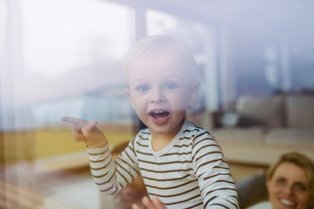 Cute boy looking out of window, laughing.の写真素材