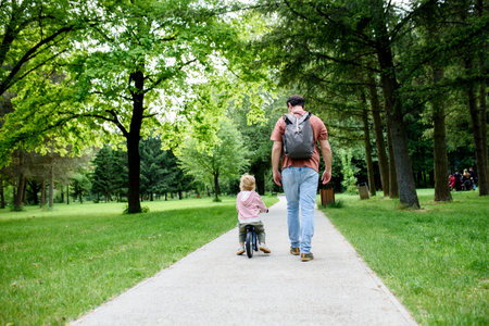 Rear view of father walking with his son across park