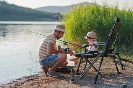 Dad teaching his little boy how to fish by the lakeの写真素材