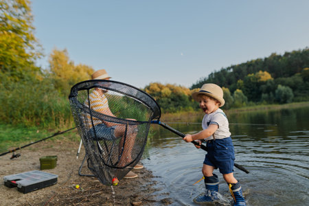 Toddler helping father with fishing net on lakeshore.の写真素材