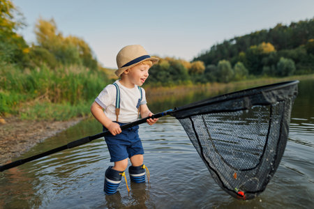 Boy standing in water with fishing net, enjoying a carefree moment in nature.の写真素材