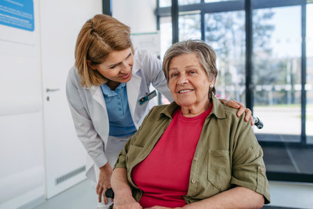 Geriatric doctor talking with patient in a wheelchair in hospital hallway.の写真素材