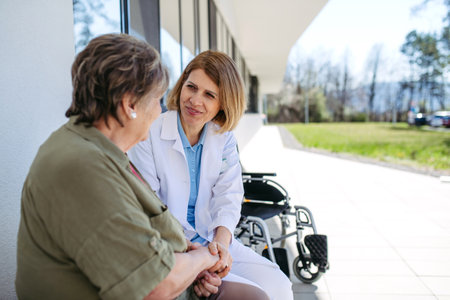 Doctor and elderly patient sitting in front of hospital building and talking.の写真素材
