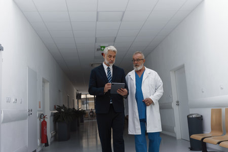 Manager walking with doctor down the hallway, showing him document in tablet.の写真素材