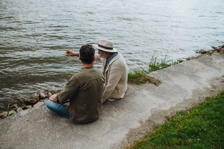 Father and adult son sharing a peaceful moment, lookign at river.の写真素材