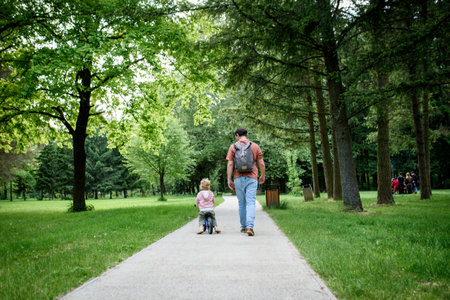 Rear view of father walking with his son across parkの写真素材
