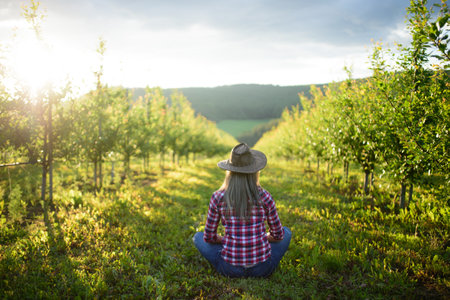 A rear view of female farmer sitting outdoors in orchard. Copy space.の写真素材