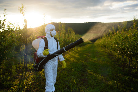 Farmer spraying pesticide in orchard, disinfecting trees in protective suit.の写真素材