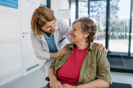 Geriatric doctor talking with patient in a wheelchair in hospital hallway.の写真素材