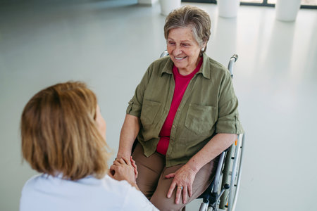 Senior woman in wheelchair smiling during conversation with caregiver.の写真素材