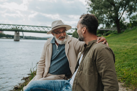 Father and adult son sharing a peaceful moment, lookign at river.の写真素材