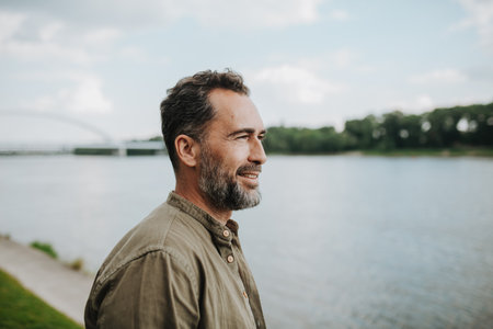 Portrait of confident middle-aged man standing on river bank, looking at water.の写真素材