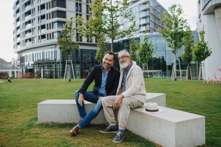 Father and adult son sitting on bench in park, sharing peaceful moment.の写真素材