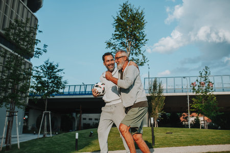 Sporty father and adult son walking home after football match in park.の写真素材
