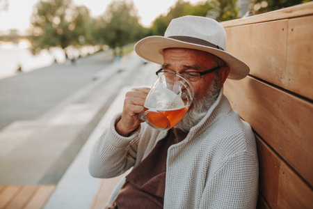 Senior man enjoying beer on sunny riverside promenadeの写真素材