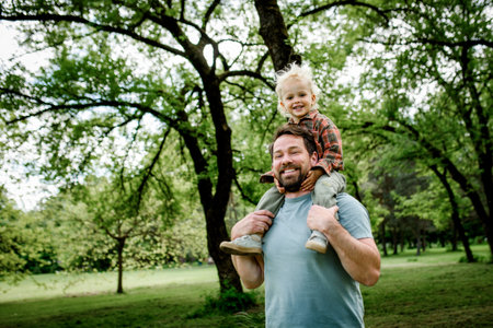 Father carrying his smiling son on shoulders during walk in parkの写真素材