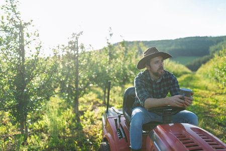 Farmer sitting on small tractor in orchard, enjoying peaceful moment.の写真素材