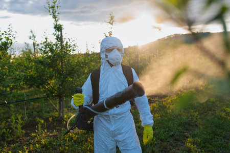 Farmer spraying pesticide in orchard, disinfecting trees in protective suit.の写真素材