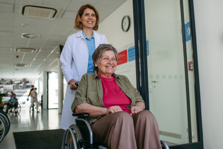 Geriatric doctor pushing a patient in a wheelchair down a hospital hallway.の写真素材