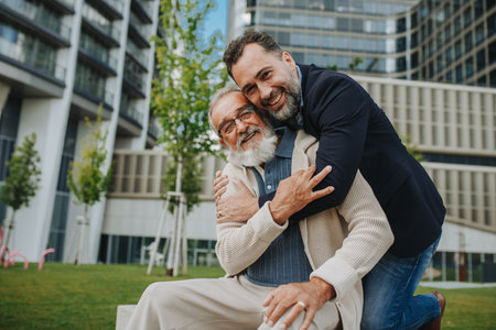 Father and adult son sitting on bench in park, sharing peaceful moment.の写真素材