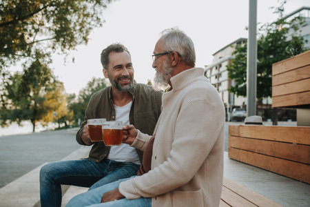 Smiling dad and adult son enjoying cold beer outdoorsの写真素材