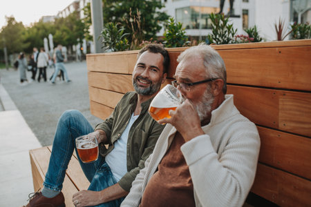 Smiling dad and adult son enjoying cold beer outdoorsの写真素材