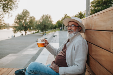 Senior man enjoying beer on sunny riverside promenadeの写真素材