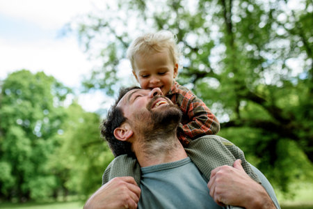 Father carrying his smiling son on shoulders during walk in parkの写真素材