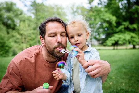 Father and son blowing soap bubbles in park.の写真素材