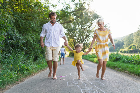 Parents helping litthe girl with hopscotch during warm summer day.の写真素材