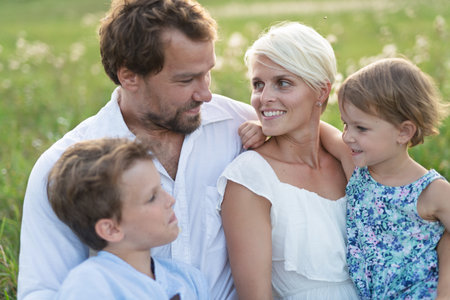 Young family with small children in summer nature at sunset, sitting in the grass.