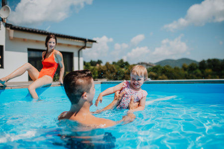 Young family with small daughter in swimming pool outdoors in backyard garden.の写真素材