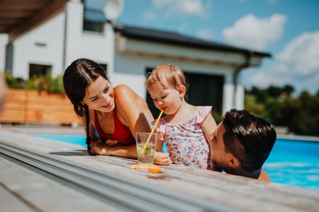 Young family with small daughter in swimming pool outdoors in backyard garden.の写真素材