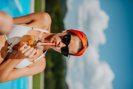 Young woman sitting by swimming pool and drinking limonade.の写真素材